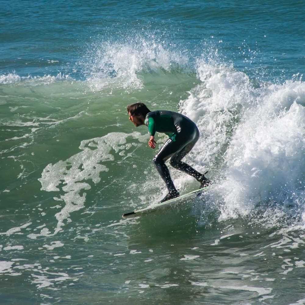 A surfer crouching on a board as a wave breaks around them
